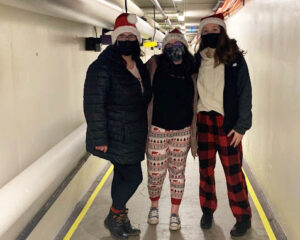 Standing in the tunnels under campus, the three are wearing holiday-patterned clothes and red Santa hats.